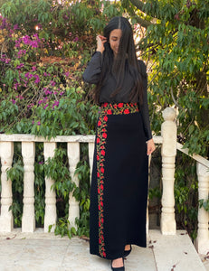Woman wearing a black dress with red floral embroidery standing outdoors.